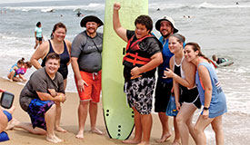 multiple generations pose around a surfboard on a beach