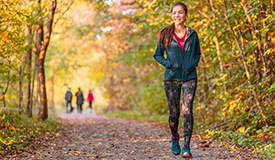 woman walks a paved wooded trail in the fall