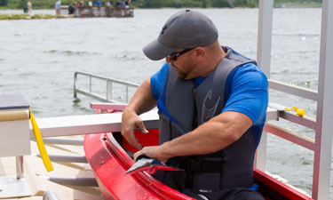 Travis Hasenkamp, who is paralyzed from the waist down, transfers without assistance from the adaptive kayak launch dock at Glenn Cunningham Lake into his kayak. 